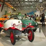 W muzeum techniki Berlin: zabytkowe samochody, w tym biało-czerwony pojazd z epoki, oraz zielony klasyk.