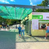 Wejście do ogrodu zoologicznego w Pradze. Ludzie stoją w kolejce do kasy biletowej pod zielonym zadaszeniem.