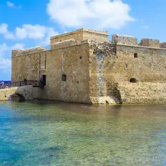 Zamek w Pafos, kamienna twierdza nad turkusową wodą, z mostem prowadzącym do wejścia.