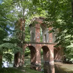 Kamienne łuki i ceglane ruiny tworzą malowniczy park romantyczny w Arkadii, otoczony bujną zielenią i spokojną wodą.