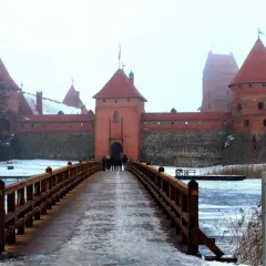 Drewniany most prowadzi do ceglanego zamku w Trokach. Zima otuliła krajobraz śniegiem i lodem.