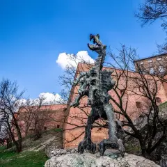 Smok Wawelski Kraków, groźny posąg smoka u stóp Wawelu, na tle ceglanych murów i błękitnego nieba.