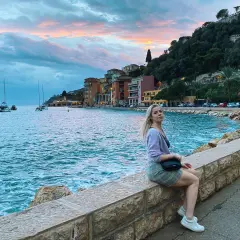 Kobieta siedzi na kamiennym murku nad morzem w Villefranche-sur-Mer, podziwiając zachód słońca i żaglówki.