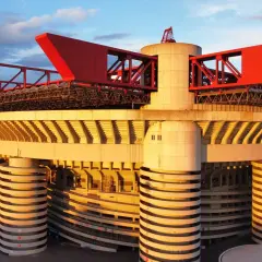 Stadion Interu Mediolan w złotym świetle zachodzącego słońca. Charakterystyczne czerwone elementy dachu i betonowe filary tworzą imponującą architekturę.