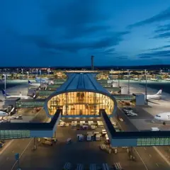 Nocny widok na port lotniczy Oslo Gardermoen z samolotami na płycie i oświetlonym terminalem.