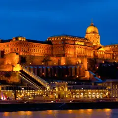 Zamek Królewski w Budapeszcie nocą, oświetlony ciepłym blaskiem, góruje nad Dunajem.