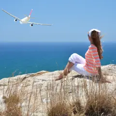 Kobieta siedzi na klifie, patrząc na samolot wznoszący się nad morzem. Widok na port lotniczy Larnaka.
