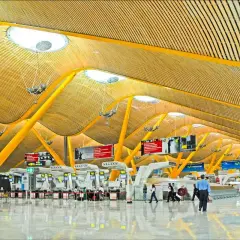 Nowoczesna architektura lotniska Madryt Barajas z charakterystycznym, falującym dachem i żółtymi podporami.