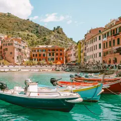 Kolorowe łodzie kołyszą się na turkusowej wodzie w malowniczym porcie Monterosso al Mare. W tle widać kolorowe kamienice i wzgórza.