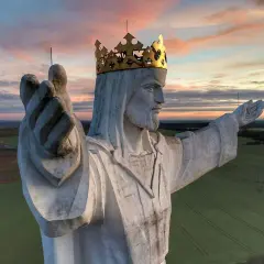 Majestatyczny pomnik Jezusa Chrystusa w złotej koronie, jeden z wielu pomników Jezusa w Polsce, wznosi się nad polami o zachodzie słońca.