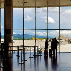 Oczekujący pasażerowie na lotnisku Mediolan Bergamo, z widokiem na samoloty i góry w tle.