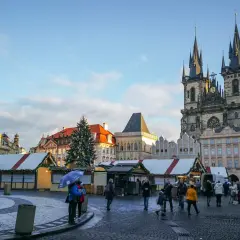 Rynek Staromiejski w Pradze, z choinką i straganami świątecznymi, podziwiany przez spacerujących ludzi.