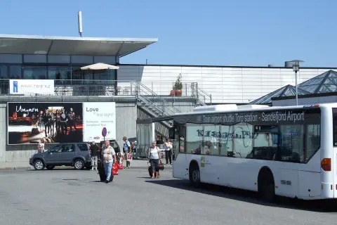Autobus wahadłowy na lotnisku Sandefjord Torp. Ludzie z bagażami czekają na transport.