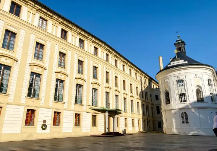 Zamek na Hradczanach, z jego żółtymi fasadami i okrągłą białą kaplicą, lśni w słońcu.