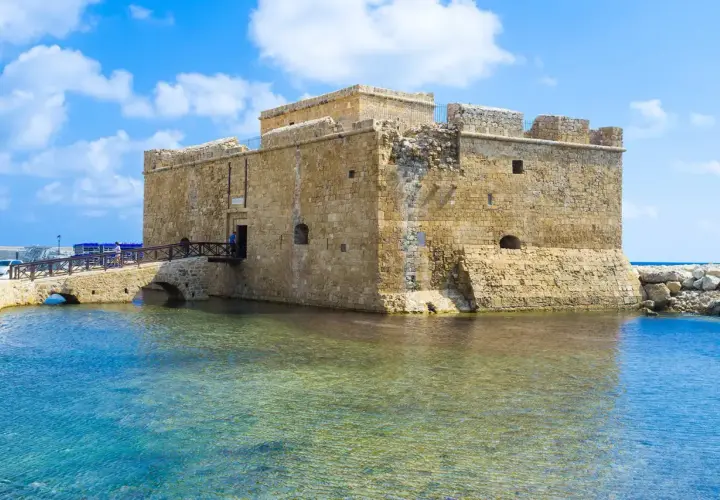 Zamek w Pafos, kamienna twierdza nad turkusową wodą, z mostem prowadzącym do wejścia.