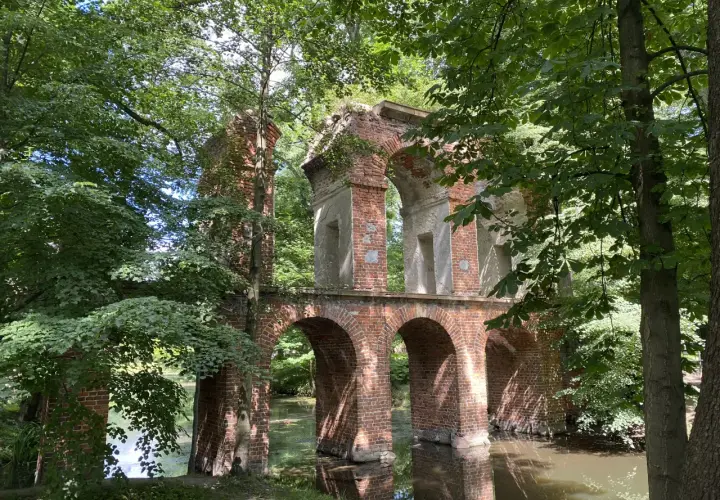Kamienne łuki i ceglane ruiny tworzą malowniczy park romantyczny w Arkadii, otoczony bujną zielenią i spokojną wodą.