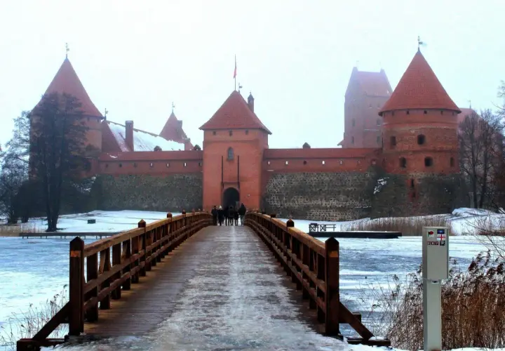 Drewniany most prowadzi do ceglanego zamku w Trokach. Zima otuliła krajobraz śniegiem i lodem.