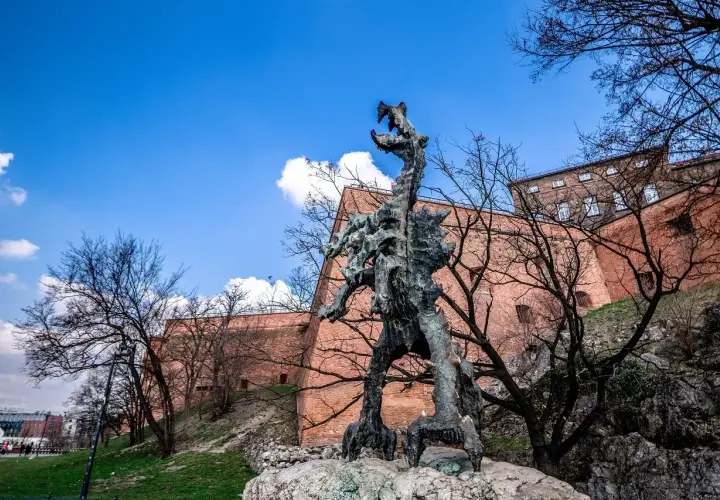 Smok Wawelski Kraków, groźny posąg smoka u stóp Wawelu, na tle ceglanych murów i błękitnego nieba.