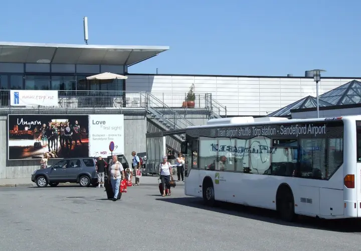 Autobus wahadłowy na lotnisku Sandefjord Torp. Ludzie z bagażami czekają na transport.