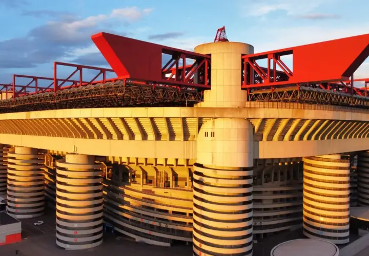 Stadion Interu Mediolan w złotym świetle zachodzącego słońca. Charakterystyczne czerwone elementy dachu i betonowe filary tworzą imponującą architekturę.