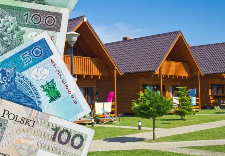 Polskie banknoty przed drewnianymi domkami letniskowymi. Zastanawiasz się, gdzie najlepiej rezerwować noclegi, by wakacje były udane i nie zrujnowały budżetu?