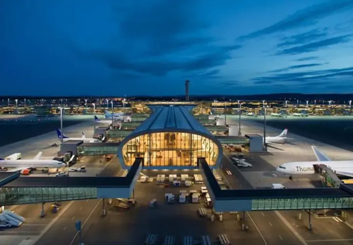 Nocny widok na port lotniczy Oslo Gardermoen z samolotami na płycie i oświetlonym terminalem.