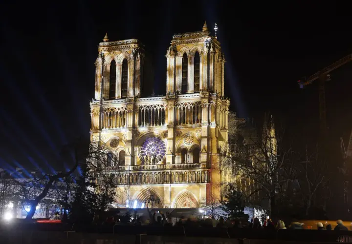 Katedra Notre Dame w Paryżu nocą, oświetlona reflektorami. Widać tłum ludzi oglądających spektakl.