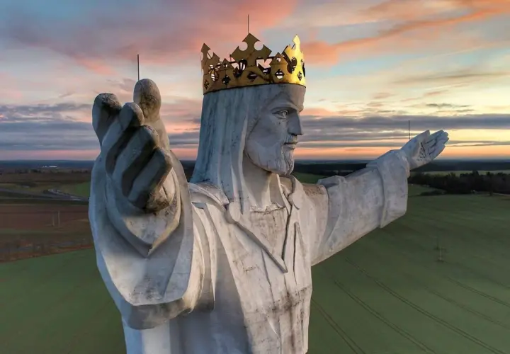 Majestatyczny pomnik Jezusa Chrystusa w złotej koronie, jeden z wielu pomników Jezusa w Polsce, wznosi się nad polami o zachodzie słońca.