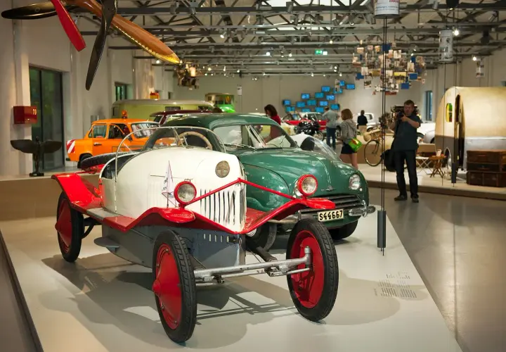 W muzeum techniki Berlin: zabytkowe samochody, w tym biało-czerwony pojazd z epoki, oraz zielony klasyk.