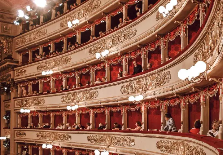 Wnętrze La Scala w Mediolanie, z widownią w lożach, ozdobione złotymi zdobieniami i czerwonymi zasłonami.