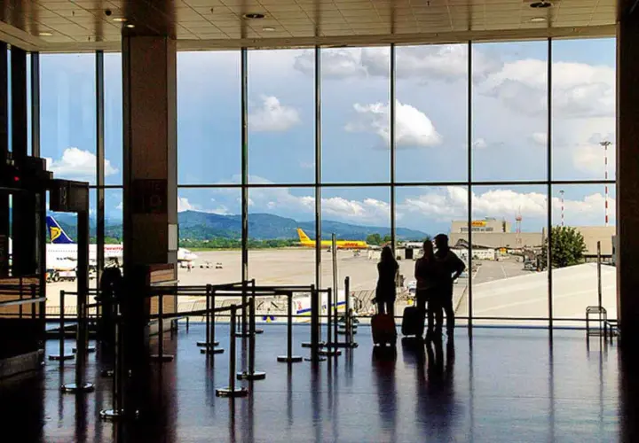 Oczekujący pasażerowie na lotnisku Mediolan Bergamo, z widokiem na samoloty i góry w tle.