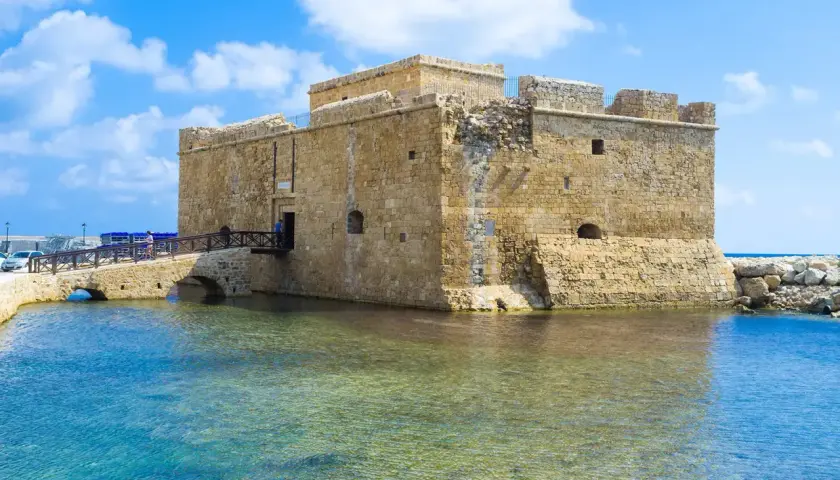 Zamek w Pafos, kamienna twierdza nad turkusową wodą, z mostem prowadzącym do wejścia.