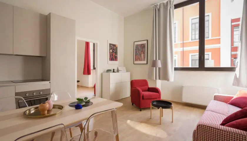 Nowoczesny apartament z kuchnią, jadalnią i salonem. Czy Airbnb jest bezpieczne? Ten przytulny pokój z czerwonym fotelem i kanapą sugeruje, że tak.