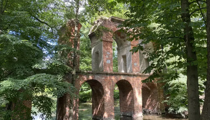 Kamienne łuki i ceglane ruiny tworzą malowniczy park romantyczny w Arkadii, otoczony bujną zielenią i spokojną wodą.