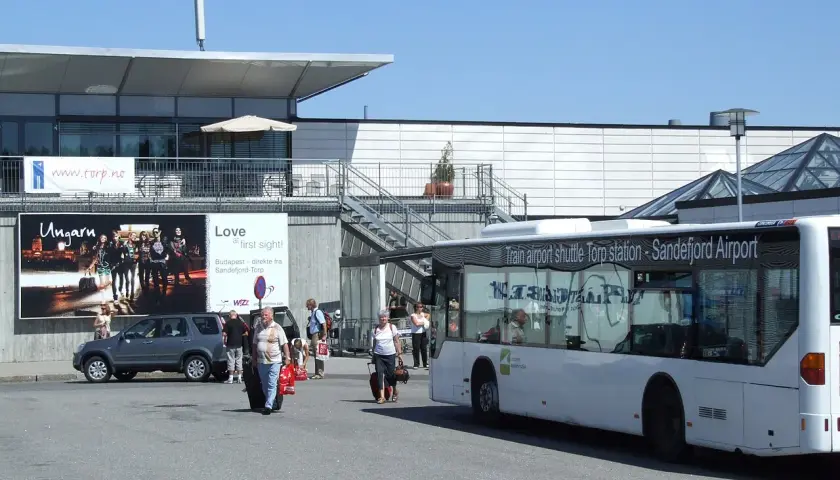 Autobus wahadłowy na lotnisku Sandefjord Torp. Ludzie z bagażami czekają na transport.