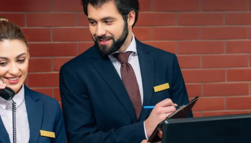 Recepcjonistka odbiera telefon, a recepcjonista notuje. Dyskretnie pytają, czy w hotelu obowiązuje cisza nocna.