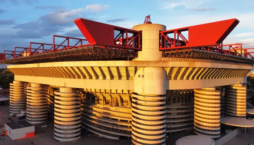 Stadion Interu Mediolan w złotym świetle zachodzącego słońca. Charakterystyczne czerwone elementy dachu i betonowe filary tworzą imponującą architekturę.