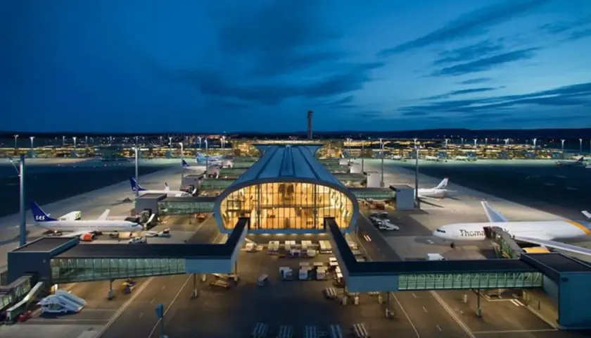 Nocny widok na port lotniczy Oslo Gardermoen z samolotami na płycie i oświetlonym terminalem.