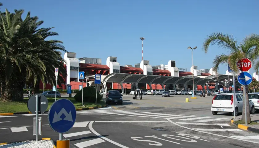 Słoneczny dzień na lotnisku Lamezia Terme. Palmy, samochody i nowoczesny budynek terminala.