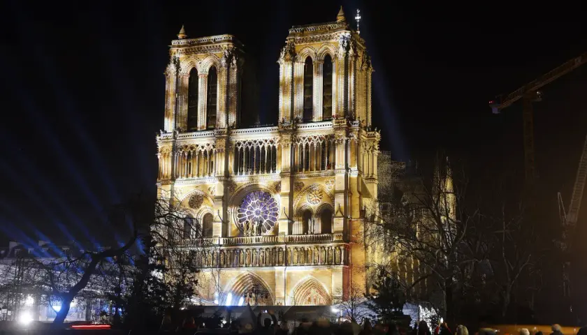 Katedra Notre Dame w Paryżu nocą, oświetlona reflektorami. Widać tłum ludzi oglądających spektakl.