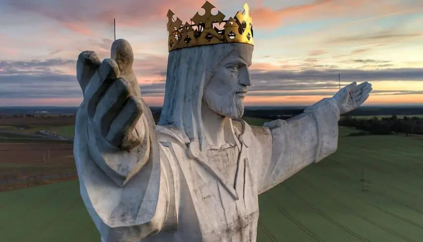 Majestatyczny pomnik Jezusa Chrystusa w złotej koronie, jeden z wielu pomników Jezusa w Polsce, wznosi się nad polami o zachodzie słońca.