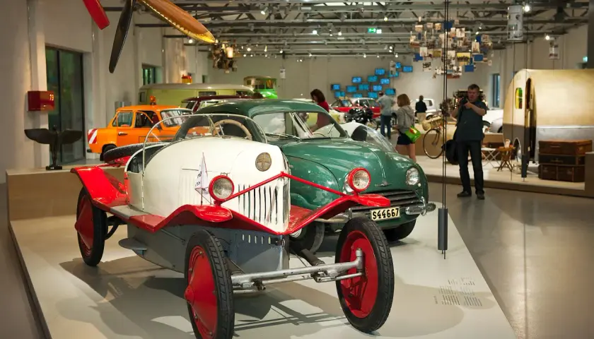 W muzeum techniki Berlin: zabytkowe samochody, w tym biało-czerwony pojazd z epoki, oraz zielony klasyk.
