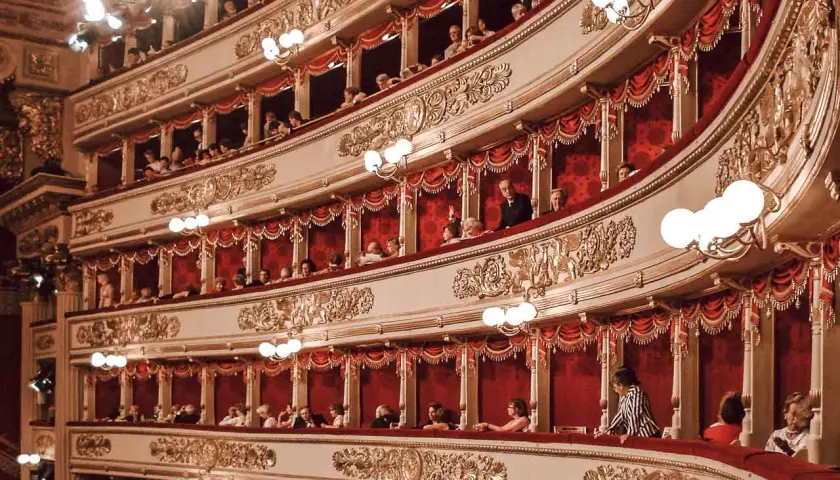 Wnętrze La Scala w Mediolanie, z widownią w lożach, ozdobione złotymi zdobieniami i czerwonymi zasłonami.