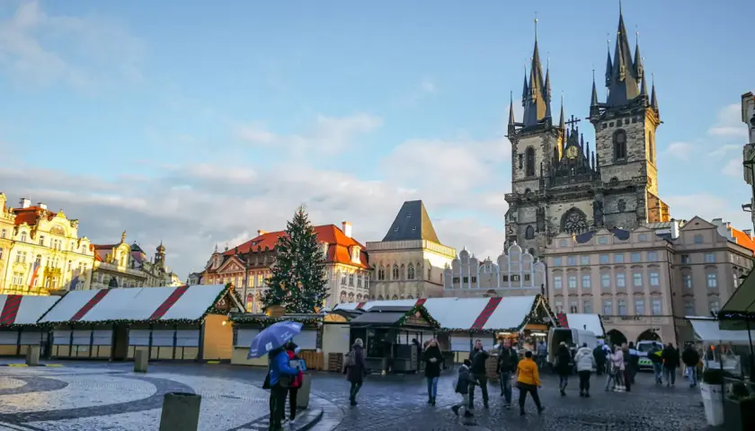 Rynek Staromiejski w Pradze, z choinką i straganami świątecznymi, podziwiany przez spacerujących ludzi.