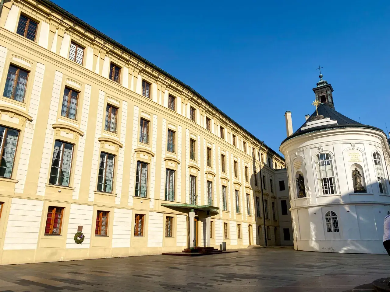 Zamek na Hradczanach, z jego żółtymi fasadami i okrągłą białą kaplicą, lśni w słońcu.