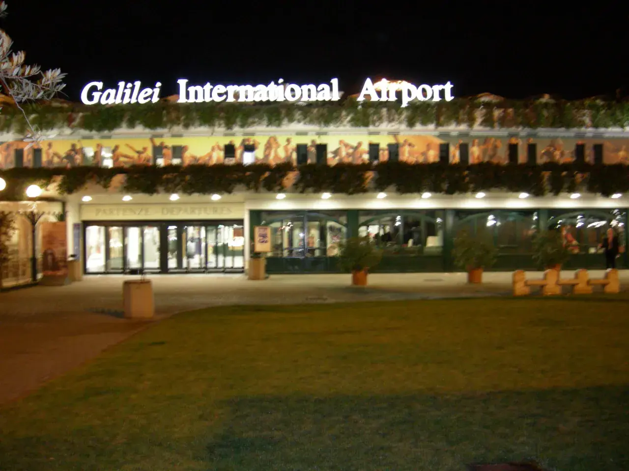 Port lotniczy Piza nocą. Jasny napis "Galilei International Airport" nad wejściem do terminalu.