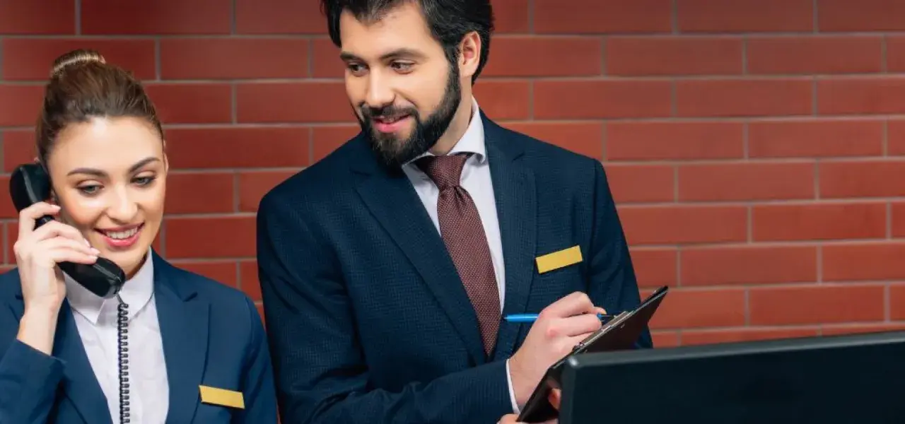 Recepcjonistka odbiera telefon, a recepcjonista notuje. Dyskretnie pytają, czy w hotelu obowiązuje cisza nocna.