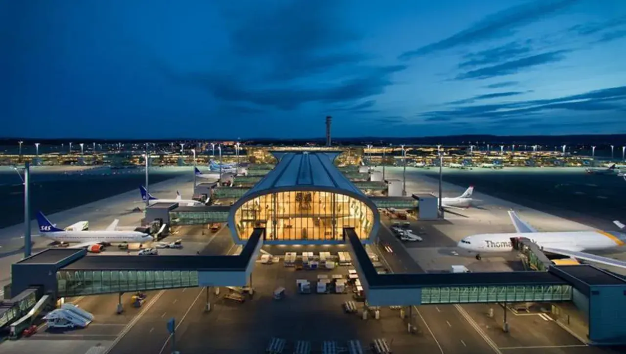 Nocny widok na port lotniczy Oslo Gardermoen z samolotami na płycie i oświetlonym terminalem.
