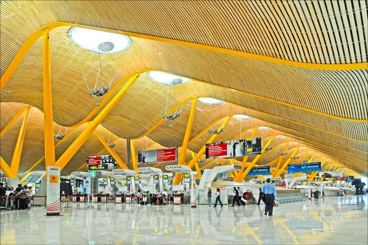 Nowoczesna architektura lotniska Madryt Barajas z charakterystycznym, falującym dachem i żółtymi podporami.