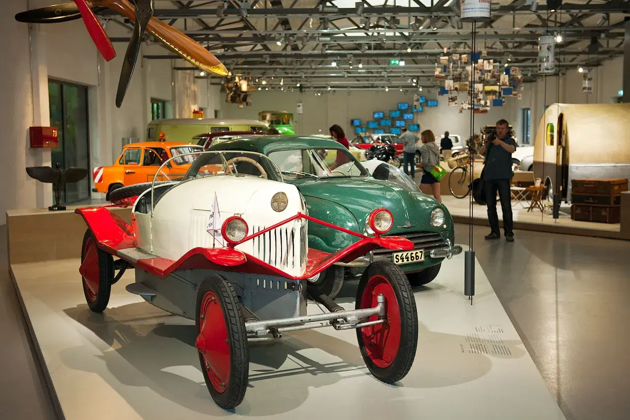 W muzeum techniki Berlin: zabytkowe samochody, w tym biało-czerwony pojazd z epoki, oraz zielony klasyk.